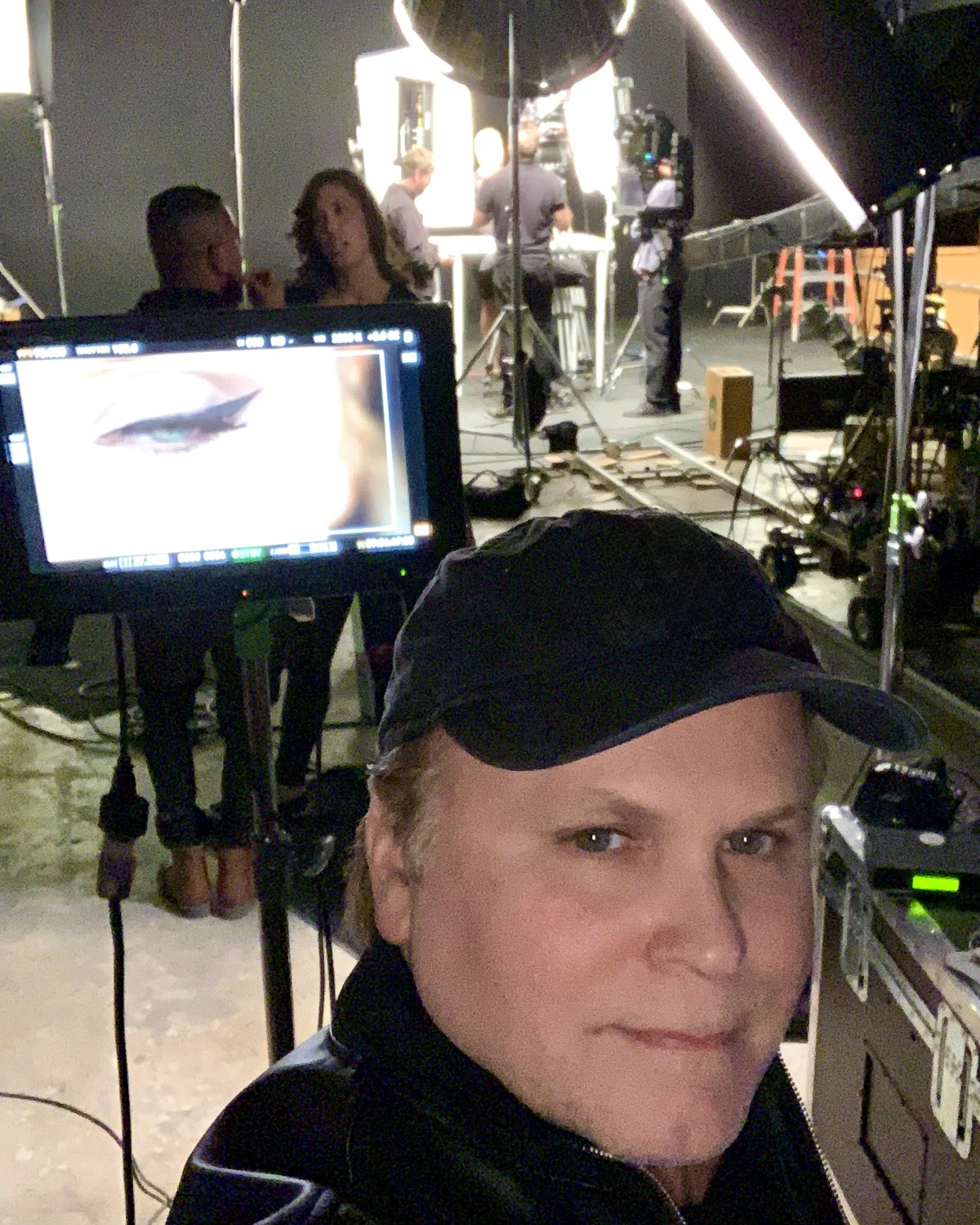 Patrick Raymond at video village on a beauty shoot, a macro eye shot on the monitor beside him and dolly track across the stage behind.